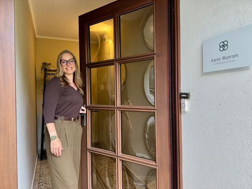 Karen Wunram mit Brille begrüßt dich an der geöffneten Praxistür